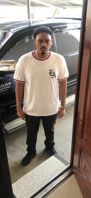 Man in cream-colored LA graphic t-shirt and black pants standing in front of a dark SUV in a garage
